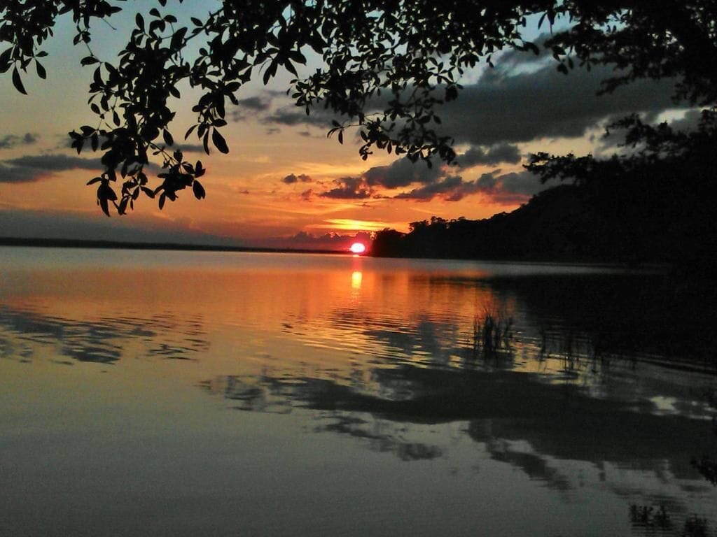 Un atardecer sobre un lago tranquilo, con reflejos del cielo.