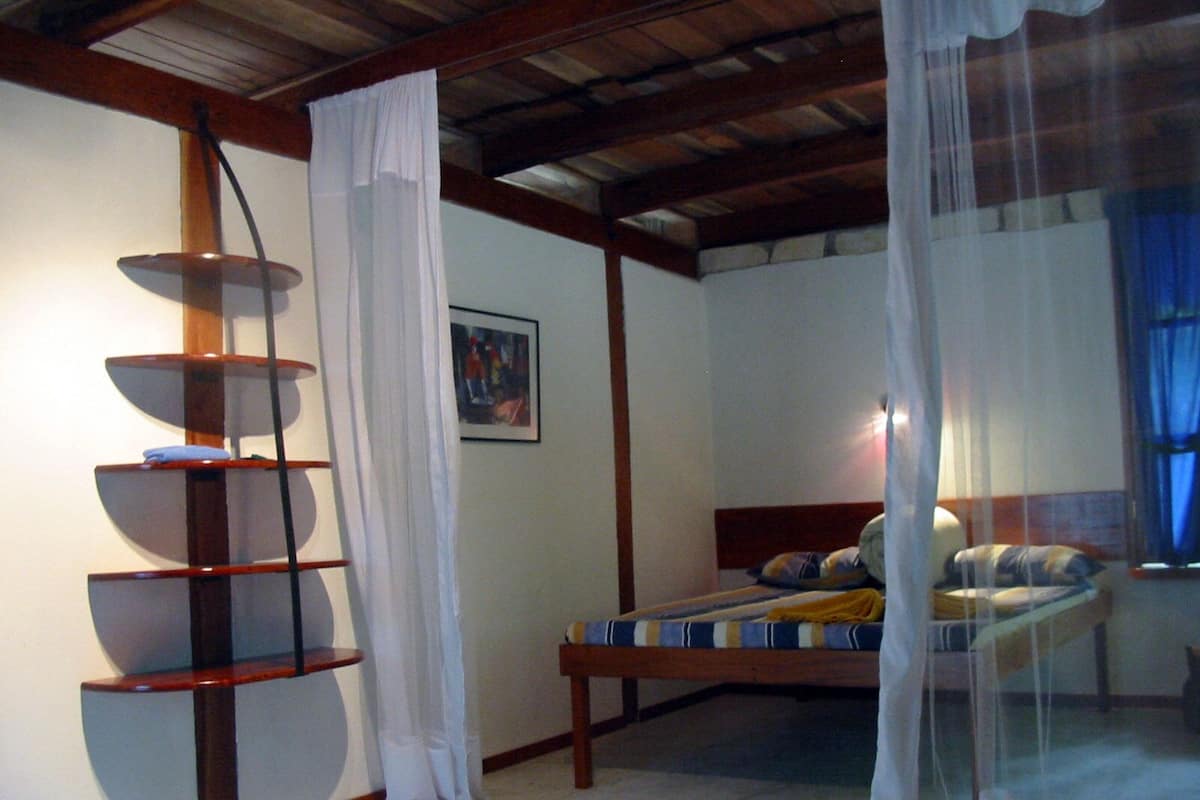 Quarto com uma cama, uma prateleira de madeira, um quadro e uma janela com cortinas.