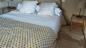 Una cama bien hecha con una colcha estampada, un cabecero redondo y dos mesitas de noche con lámparas.