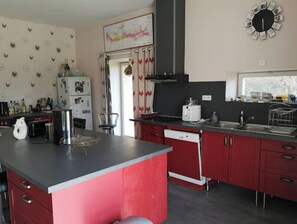 Una cocina moderna con armarios rojos, encimera negra y una isla grande. Hay un refrigerador, un microondas y un fregadero.