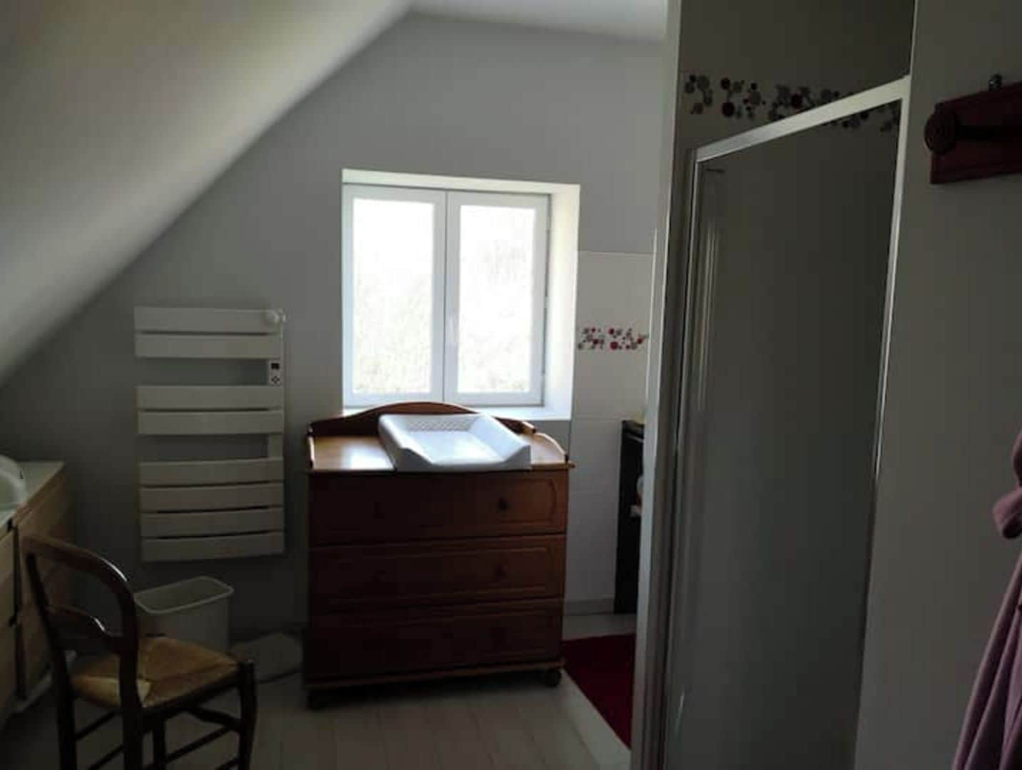 Een slaapkamer met een schuine plafond, een houten dressoir, een stoel en een raam.