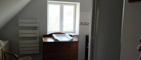 Een slaapkamer met een schuine plafond, een houten dressoir, een stoel en een raam.