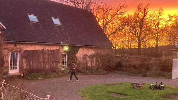 Una casa rústica con techo inclinado, entrada pavimentada y un pequeño jardín.