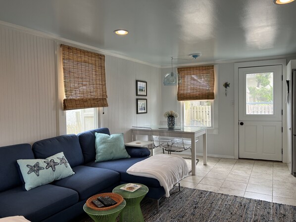 A modern living room with a dark blue sofa, a glass dining table, and a white door. - Ocean View Cottage w/ Shared "Private" Beach #1 (Point Pleasant Beach)