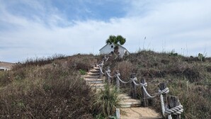 Eine Treppe führt zu einem Haus, das von trockener Vegetation umgeben ist, mit blauem Himmel.