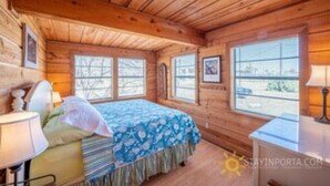 Ein Zimmer in einer Holzhütte mit einem Bett, einem Schreibtisch und großen Fenstern.