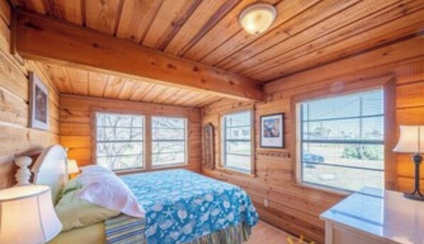 A wooden cabin room with a bed, a desk, and large windows. - Chapel Cottage, 3 BR, 2BA, sleeps 10. Walk to the Beach (Port Aransas)
