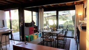 A spacious dining area with a large table and chairs, a kitchen area with a counter and cabinets, and a view of the outdoors through large windows. - Beautiful 67 m² duplex with garden.golf view (Moliets-et-Maa)