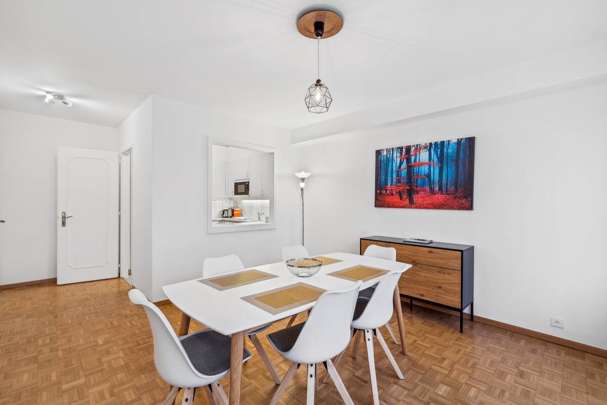 A modern dining area with a white table, four chairs, and a wooden floor.