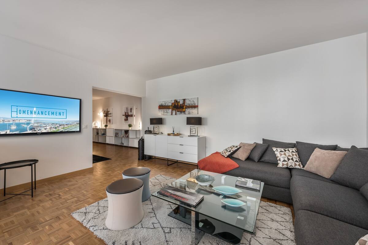 A modern living room with a large flat-screen TV, a grey sofa, a glass coffee table, and a white cabinet.