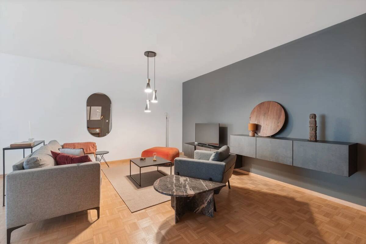 A modern living room with a grey sofa, a blue armchair, a round coffee table, and a TV on a stand.