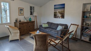 A living room with a sofa, a wicker chair, a small table, a bookshelf, and a painting on the wall.