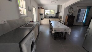 A modern kitchen with a built-in washing machine, a dining area with a table and chairs, and a large clock on the wall.