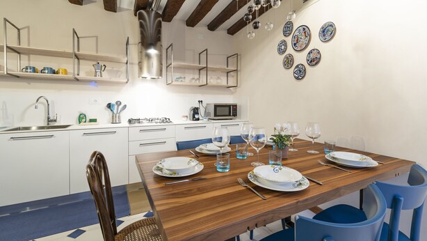 A dining area with a wooden table set for four, white plates, and blue chairs. - SAN SILVESTRO HOUSE VENICE FIRST FLOOR (Venezia)