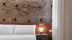 A bed with white linens, a nightstand with a lamp, and a brick wall behind. - SAN SILVESTRO HOUSE VENICE FIRST FLOOR (Venezia)