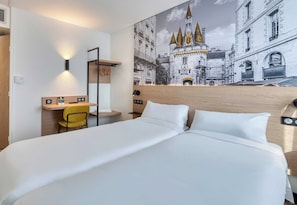 A hotel room with a large bed, a desk with a chair, a wall-mounted light, and a mural of a castle.