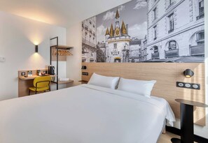 Ein Hotelzimmer mit einem großen Bett, einem Schreibtisch mit Stuhl, einem Wandregal und einem großen Wandteppich.