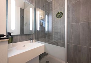 Une salle de bain moderne avec un lavabo blanc, un grand miroir et un espace douche doté d’une porte en verre perforé.