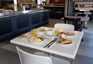 Une table de petit-déjeuner avec des assiettes remplies de nourriture, un verre de jus d’orange et une bouteille de lait.