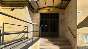 Udendørs trapper fører til en portindgang med en gul mur og gelænder af metal.