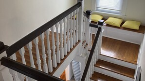 A staircase with white balusters and a dark handrail, leading to a landing with a window and a yellow cushion.