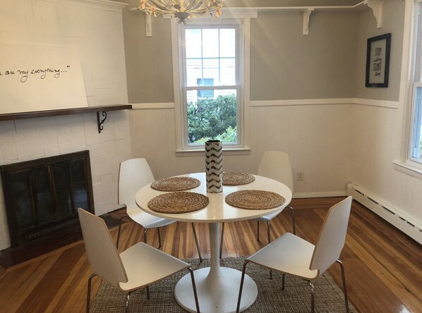 Un comedor con una mesa redonda, sillas blancas y un jarrón decorativo.