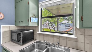 Een keuken met een magnetron, een dubbele spoelbak en een raam met uitzicht op een meer en gebouwen.