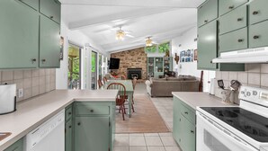 Een ruime keuken met groene kastjes, een eethoek met een tafel en stoelen, een stenen openhaard en een zithoek met een bank.