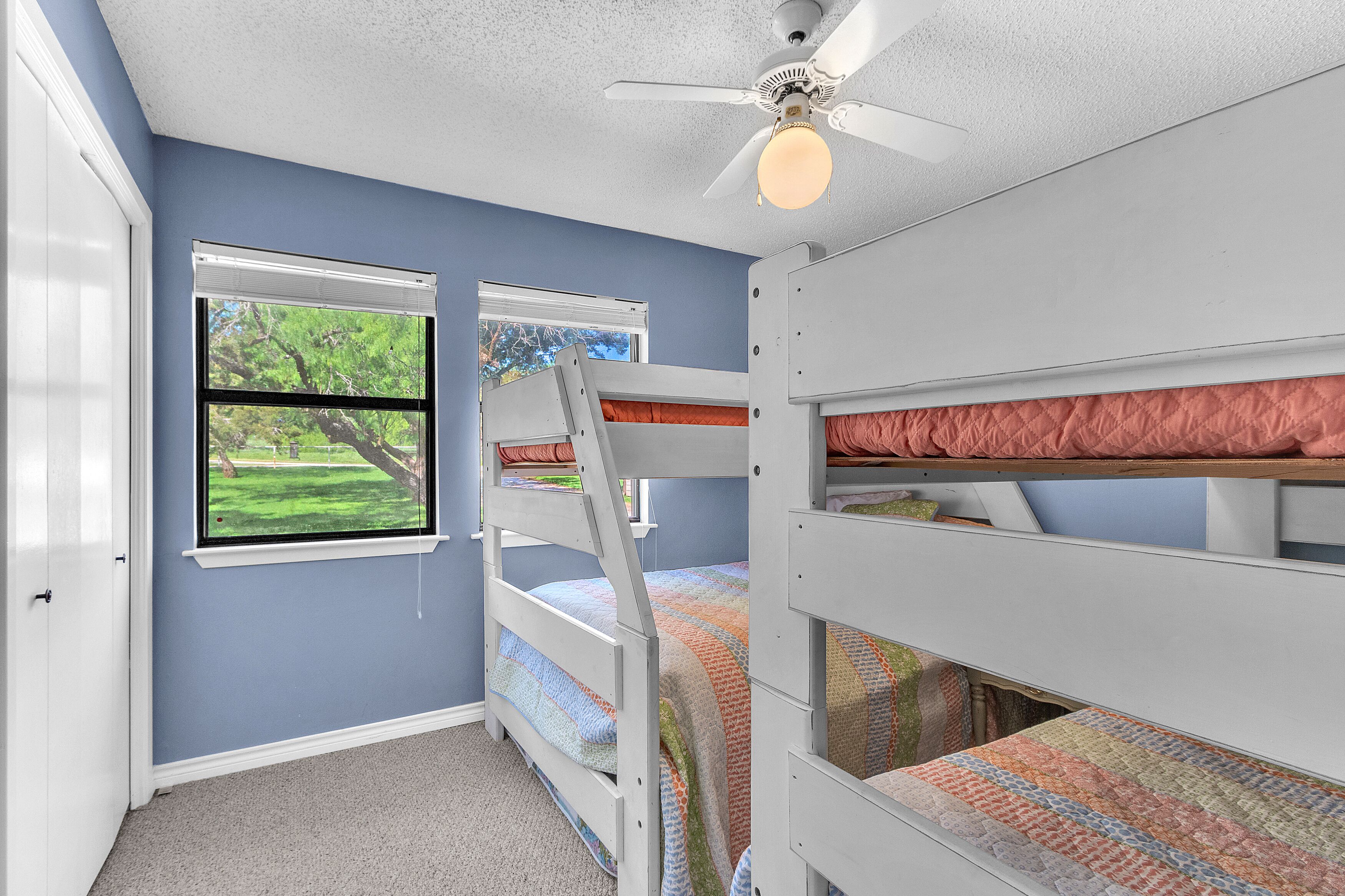 Un dormitorio con tres literas, un ventilador de techo y una ventana con vistas a un paisaje verde.