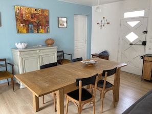 Un coin repas avec une table et des chaises en bois, un meuble blanc, un tableau au mur et une porte avec une fenêtre.