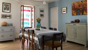 A dining area with a table set for two, a vase with flowers, and a cabinet with decorative items.