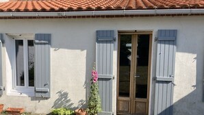 A house with a tiled roof, white walls, and grey shutters. There is a door and a window visible.