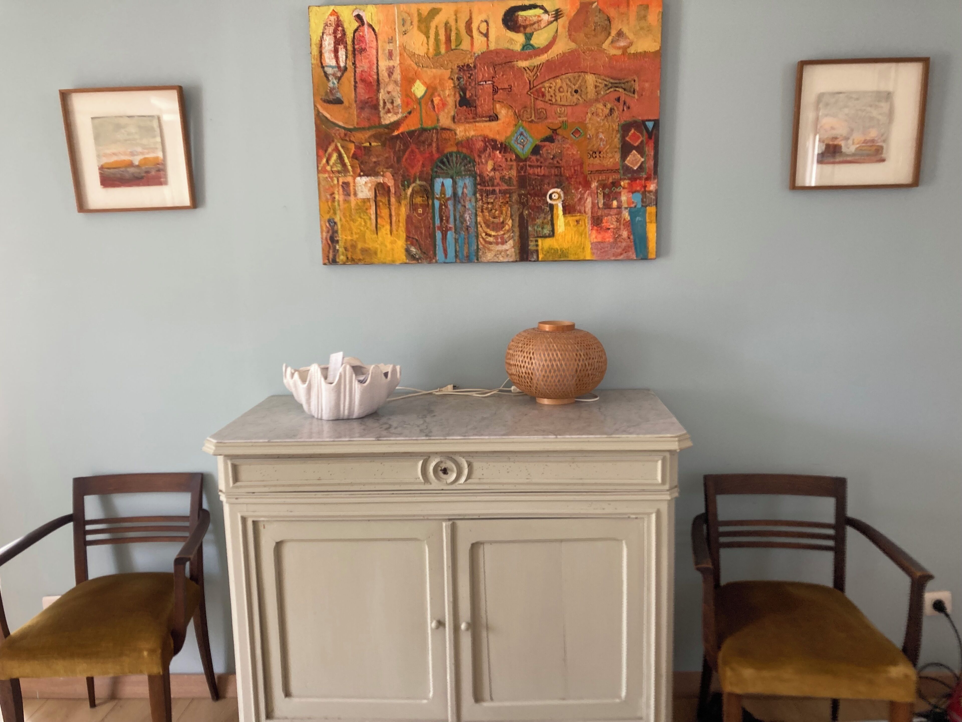 A room with a marble-top cabinet, two wooden chairs, and a colorful abstract painting on the wall.