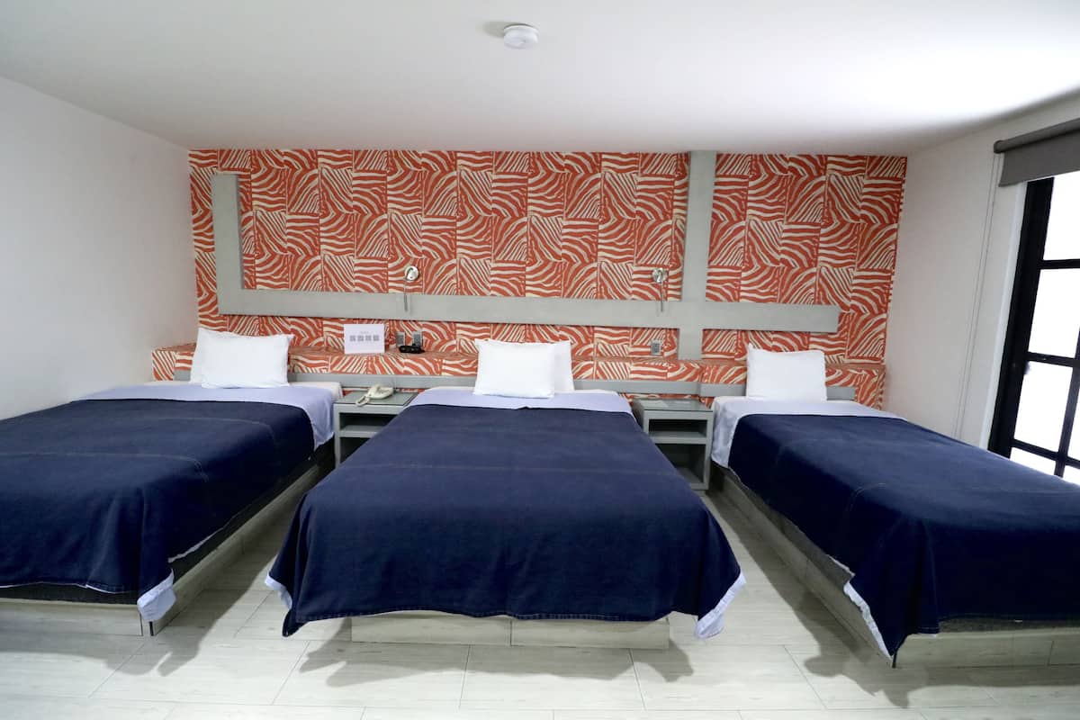 Habitación de hotel con tres camas individuales, un espejo grande y un papel tapiz estampado.