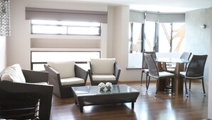 Ein modernes Wohnzimmer mit einem Glastisch, Korbmöbeln und einem Essbereich mit rundem Tisch und Stühlen.