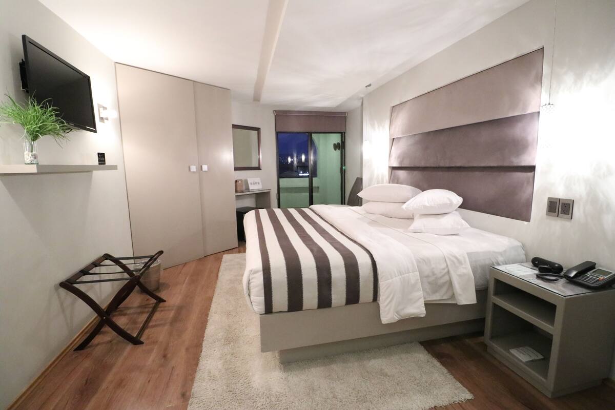 Un dormitorio moderno con cama, mesita de noche y televisor montado en la pared.