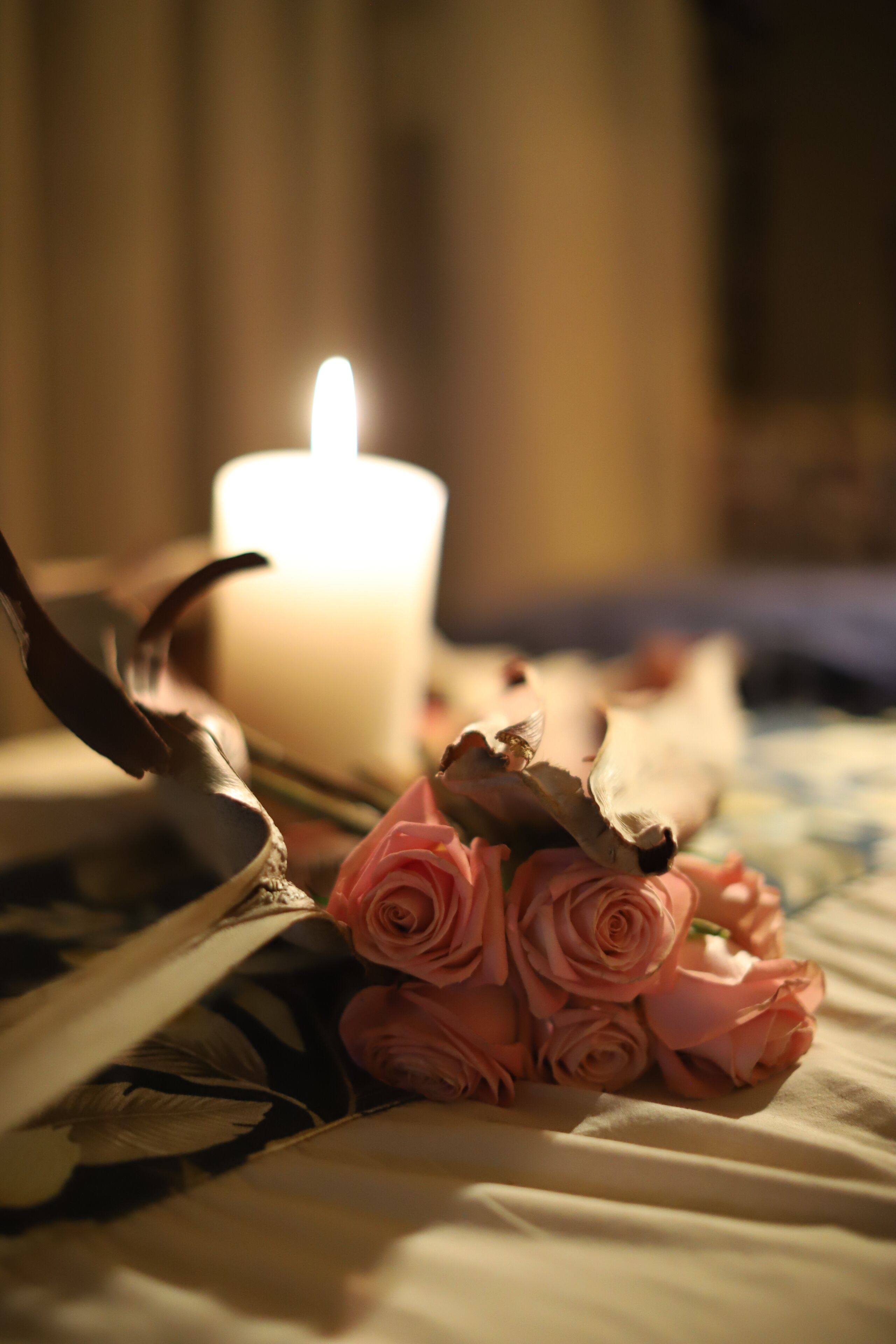 A candle, dried roses, and a feather on a bed.