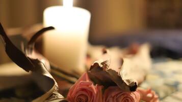 A candle, dried roses, and a feather on a bed.