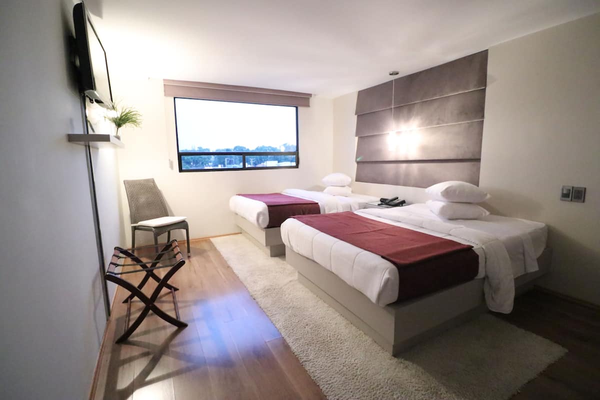 Un dormitorio moderno con dos camas, un ventanal grande, una silla y un televisor de pantalla plana montado en la pared.
