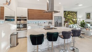 Een moderne keuken met roestvrijstalen apparatuur, een centraal eiland met barstoelen, en een groot raam met uitzicht op groen.