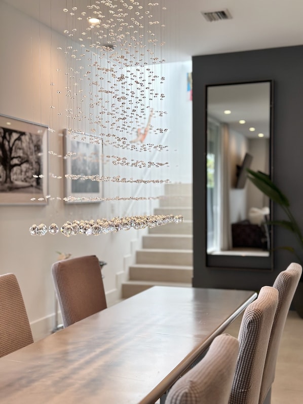 A dining area with a long table, chairs, and a hanging light fixture with crystals.