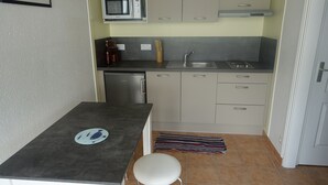 Une cuisine compacte équipée d’un four à micro-ondes, d’un évier et d’un petit réfrigérateur. On y trouve un tabouret blanc et un tapis à motifs sur le sol.