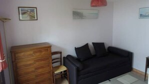 Une pièce avec un canapé noir, une commode en bois et un luminaire suspendu rouge.