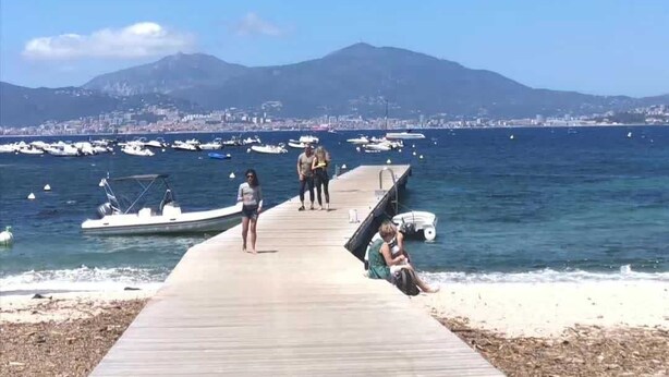 A wooden pier leading to a beach with boats in the water and a mountain in the background.
