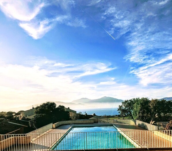 A rectangular pool with a metal railing, surrounded by a wooden deck, set against a backdrop of mountains and a clear sky.