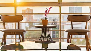 Une pièce avec une table et deux chaises, disposées face à une grande fenêtre donnant sur des immeubles.