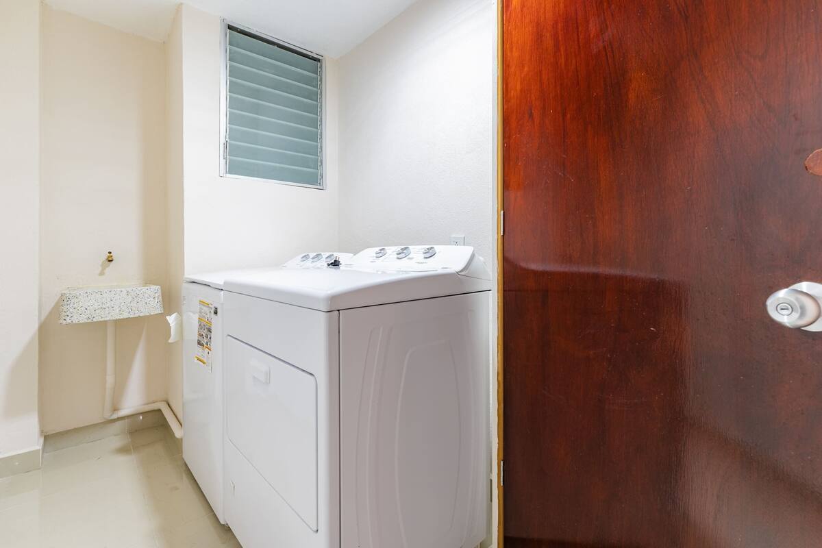 A laundry room with a washing machine, a dryer, a window with blinds, and a wooden door.