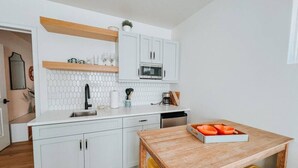 Una cocina compacta con armarios blancos, un microondas y una mesa de comedor de madera con sillas amarillas.