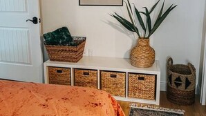 Un dormitorio con cama, mesita de noche con cestas, espejo y decoración mural.