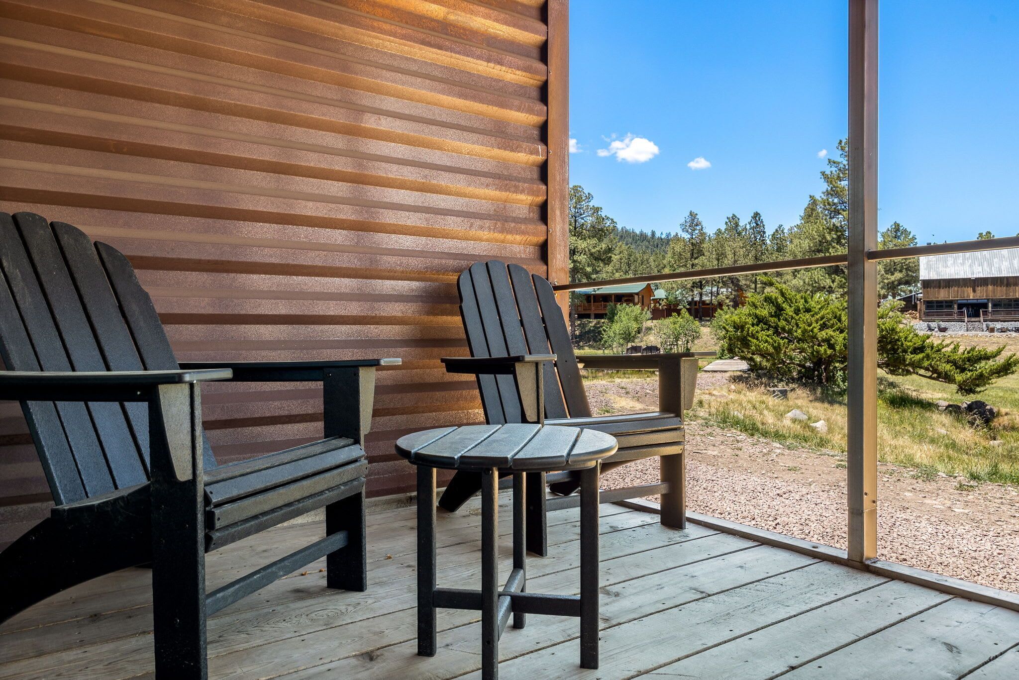 A wooden deck with two Adirondack chairs and a small table, overlooking a forested area.